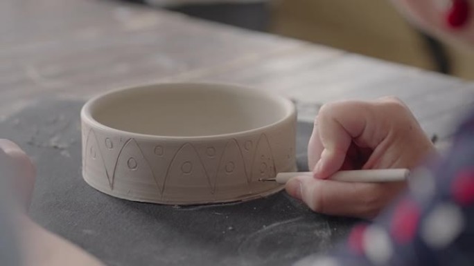 女人在陶瓷板上绘画时的手。制作手工粘土菜肴的波特车间。艺术家在陶器车间在陶器上创造了美丽的图案。特写