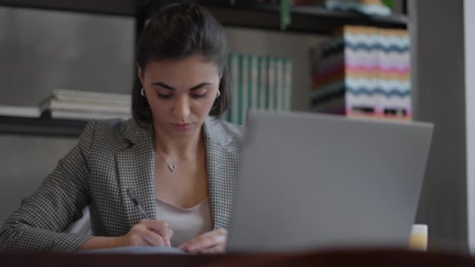 女商人分析图表并在笔记本电脑上打字。远程工作，戴眼镜的年轻女性在剪贴板上写笔记，在笔记本电脑键盘上打