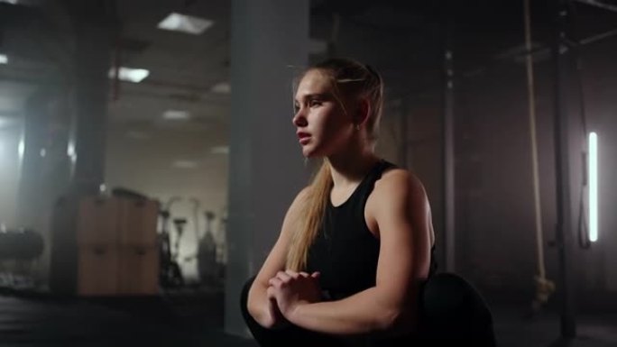一名年轻苗条的女子在训练前准备和热身。在黑暗的健身室内进行单调的艰苦锻炼后，拉紧和伸展肌肉