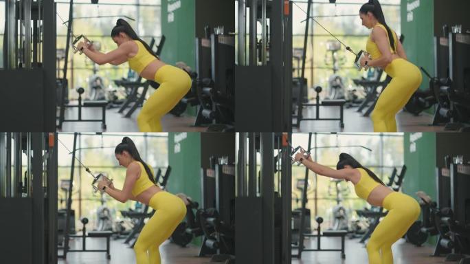 一位穿着黄色运动服的年轻西班牙裔妇女在跨界运动中进行锻炼，从上方拉出一根钢绳来训练她的背部和肩膀。一