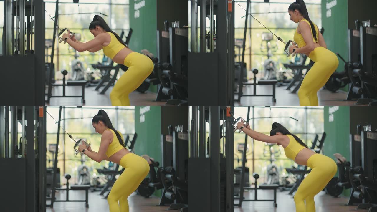 一位穿着黄色运动服的年轻西班牙裔妇女在跨界运动中进行锻炼，从上方拉出一根钢绳来训练她的背部和肩膀。一