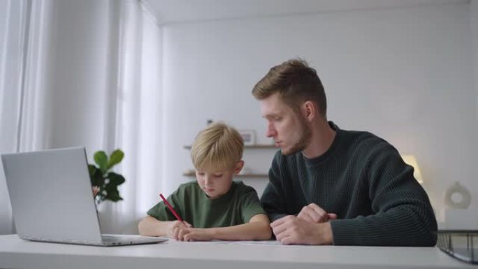 父子俩一起做作业，坐在客厅的桌子旁，看着笔记本电脑的屏幕。父亲身份。关爱现代父母的理念。远程教育