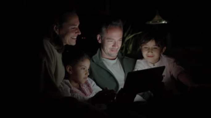 可爱的四口之家晚上在平板电脑上看电影，看起来都很开心