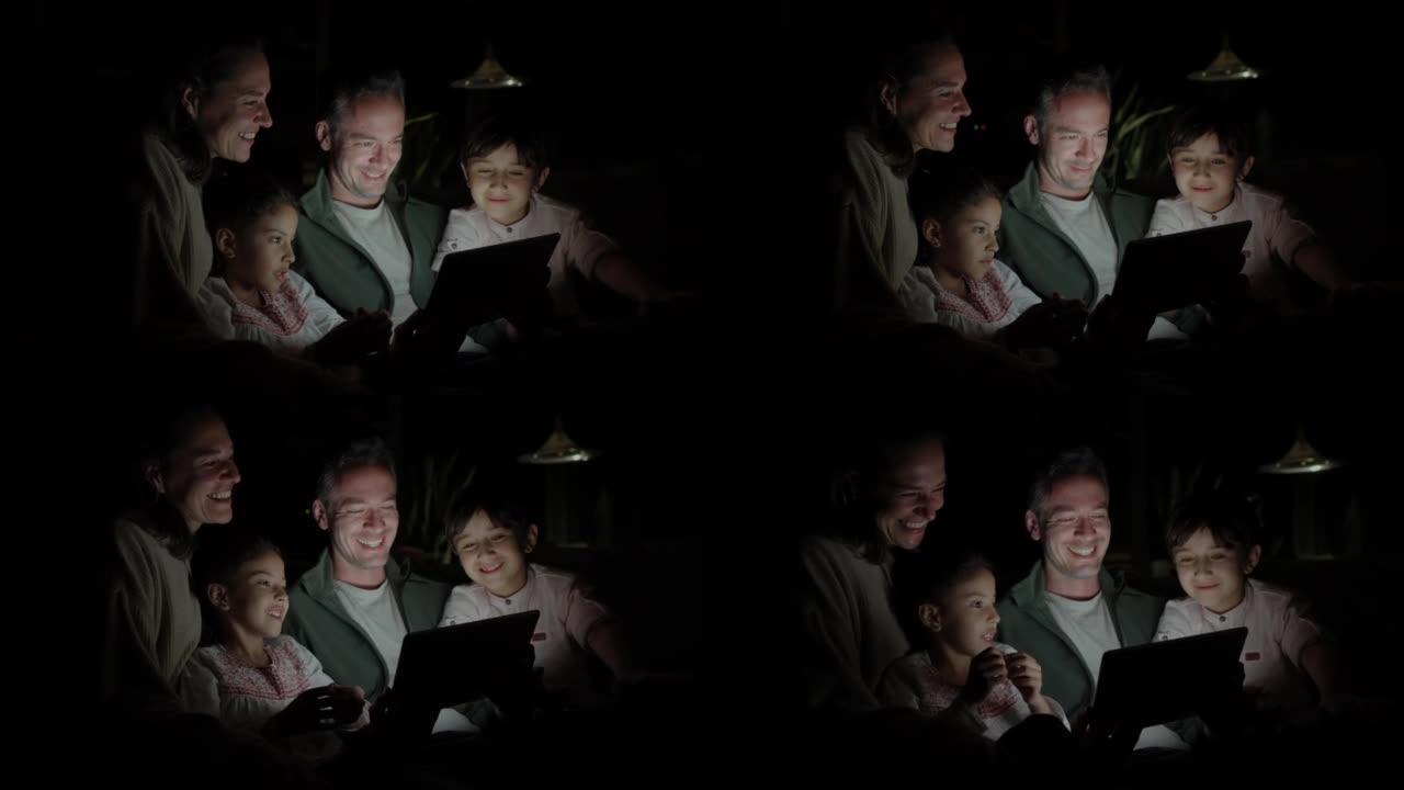 可爱的四口之家晚上在平板电脑上看电影，看起来都很开心