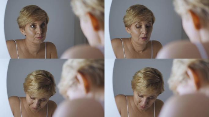 沮丧的不满意的女人在她的第45个悲伤地看着镜子，对自己失去信心和生活动力，中年危机，更年期的发作