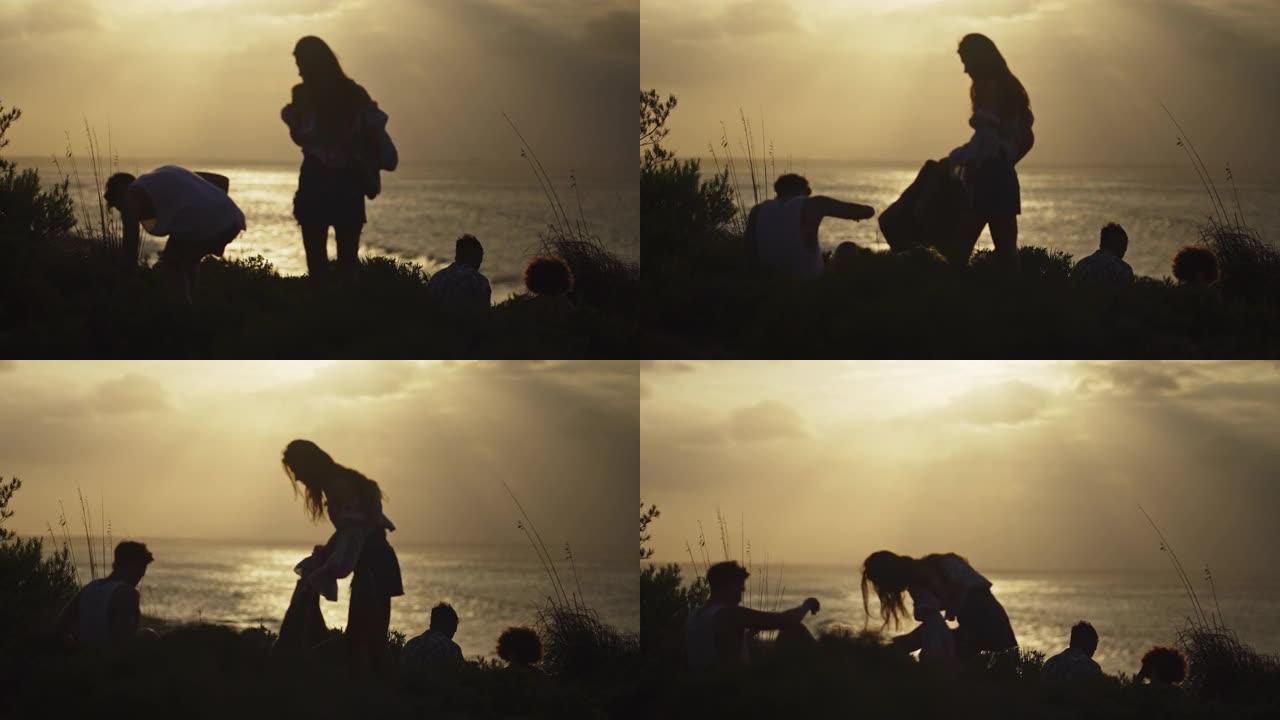 一群不同的朋友坐在绿草如茵的悬崖上，看着海上的日落。一起露营