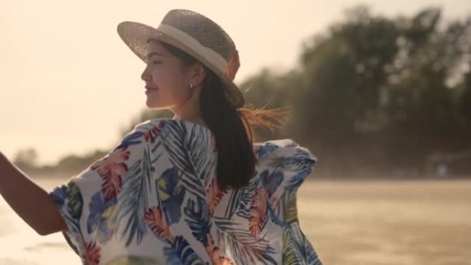 使用智能手机的亚洲妇女在日落时在海滩上自拍。