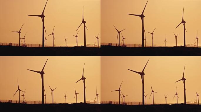 夕阳下，风力涡轮机矗立在犁过的田野上。