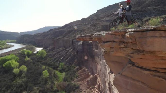 山地自行车夫妇在河上的峡谷边缘暂停，日出