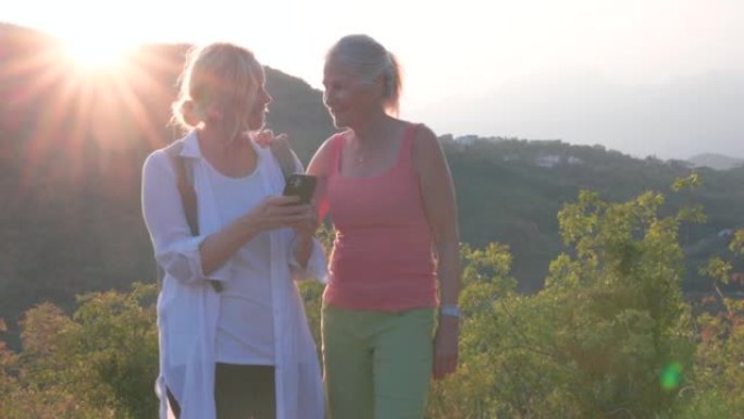 两名高级妇女在远足时在希尔克雷斯特 (hill crest) 停下来，看看智能手机