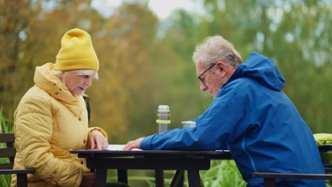 老年夫妇看着地图休息一下，在公园的桌子上喝茶