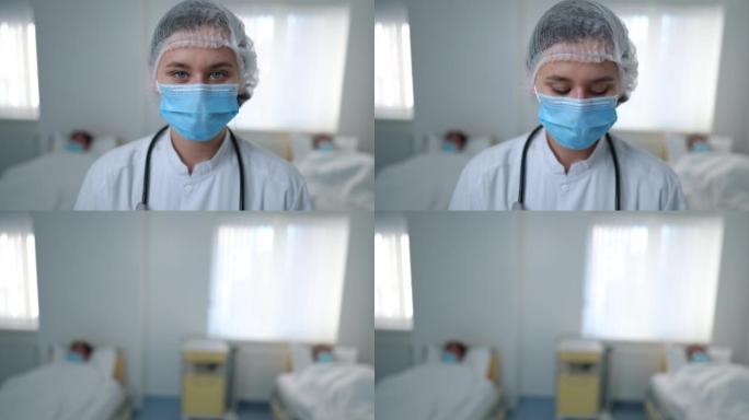 穿着冠状病毒制服的特写女人看着相机离开医院病房，背景是病人。戴着口罩的年轻白人医生走开了。新型冠状病