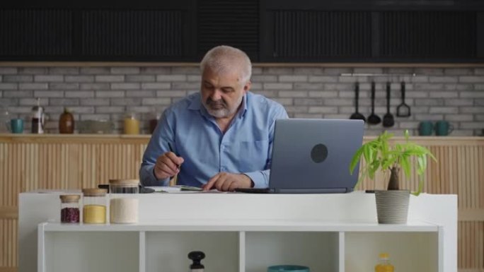 老人正在检查水电费，在网上计算和付款，使用笔记本电脑，坐在家里的厨房里