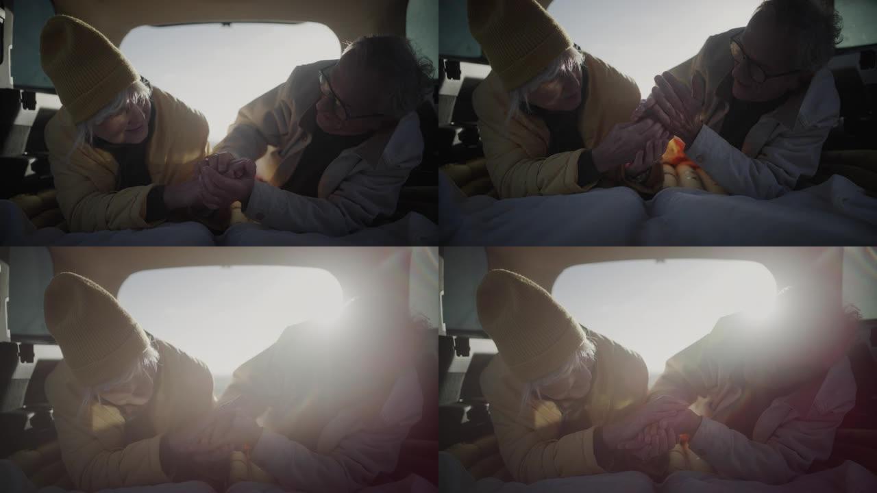 两个老年人在公路旅行中露营。躺在大型汽车后备箱中互相温暖