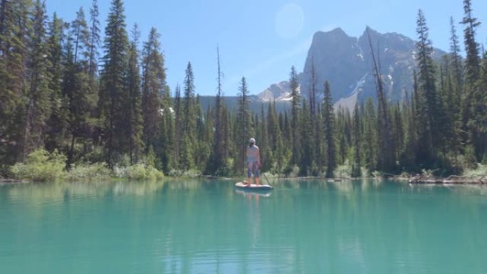 女人划桨在宁静的山湖上站起来划桨板