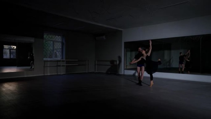 极宽镜头舞蹈工作室，年轻男子旋转女子在阿拉伯风格的位置在右边。高加索夫妇的芭蕾舞演员在室内黑暗中排练