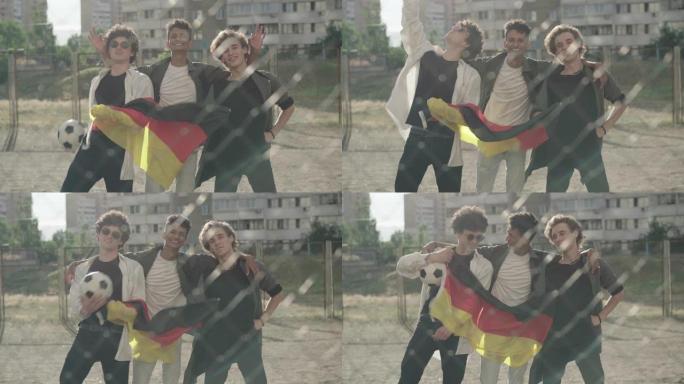 三个快乐的多民族朋友在网状围栏后面与运动球和德国国旗合影。欢快的年轻人庆祝东德和西德1989年团聚的