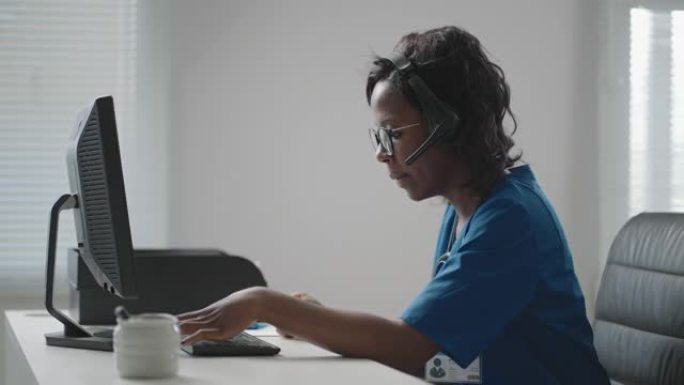穿着白大褂的非洲裔美国黑人女性全科医生坐在医生办公室的办公桌前，一边滚动电脑鼠标，一边阅读病人的病史