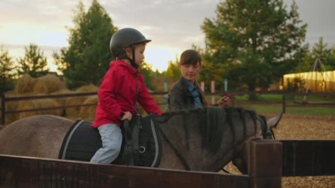 可爱的小男孩在小马俱乐部为孩子们训练，蹒跚学步的孩子在教练的帮助下骑马，运动爱好