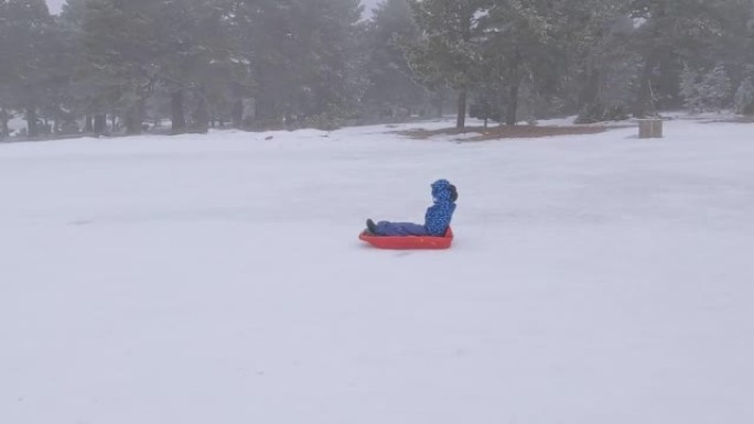 在下雪天，傲慢的男孩手放在脖子后面，滑下滑雪橇
