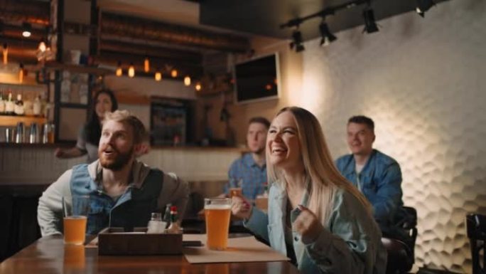 观看体育比赛时，高加索男女朋友在bar ro pub欢呼雀跃。足球迷用啤酒和小吃在电视上观看比赛。