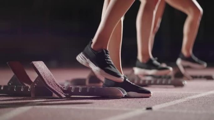 在起跑线附近的黑暗中，穿着运动鞋的女跑步者的腿特写，比赛的准备和准备