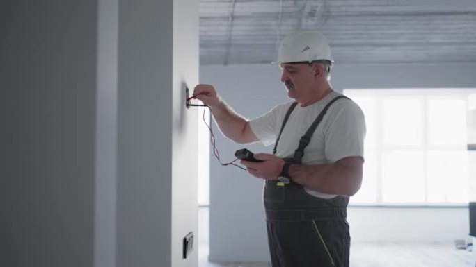 一名男性电工用电线测试仪检查网络中的电压，准备在建筑工地上安装智能房屋。