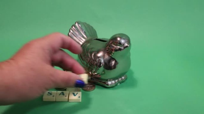 成年女性手把“储蓄”字放在旁边的鸟形储蓄罐和硬币对号入座