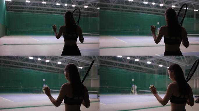 年轻的黑发女子在室内的网球场上行走，投掷球并接球，准备发球。