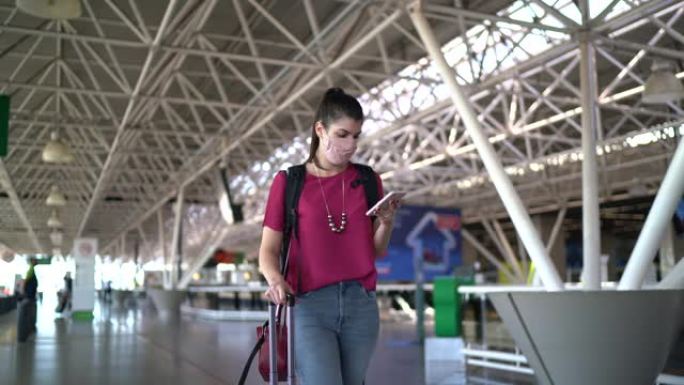 年轻的旅行者妇女在机场走路和使用电话-戴着口罩