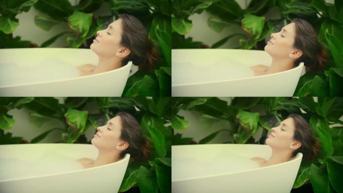 年轻女子在浴室内郁郁葱葱的绿色花园里洗泡泡浴。脸部特写