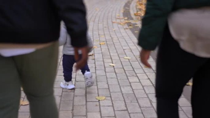 后视图自信的古玩小男孩和面目全非的父母走在公园小巷上。轻松的非洲裔美国小儿子与父母一起在户外散步。