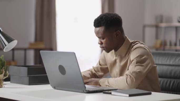 年轻的黑人正在网上学习，在笔记本电脑上观看学习视频，并在笔记本电脑上做笔记，进行自我教育