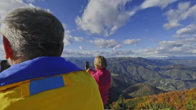 SLO MO高级男徒步旅行者用智能手机从阳光明媚的山顶拍照