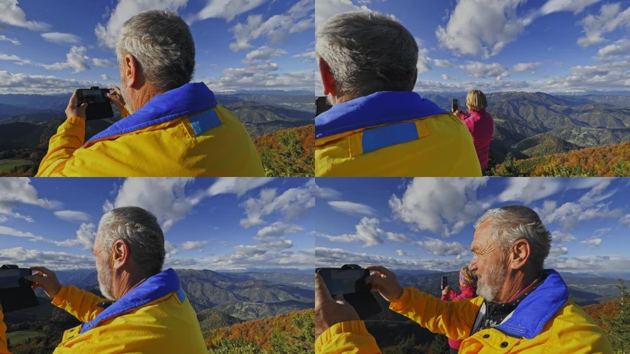 SLO MO高级男徒步旅行者用智能手机从阳光明媚的山顶拍照