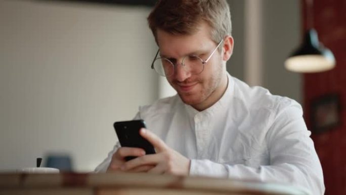戴着眼镜的年轻人在咖啡馆休息，用手机在社交网络上聊天，免费无限wifi