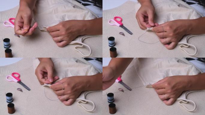 裁缝的手在用布料工作。母亲用手为她的小女儿缝了一件漂亮的衣服，特写镜头。女人用蓝线手工缝制接缝。