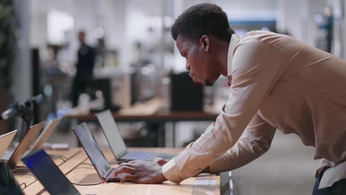 成年黑人正在购买笔记本电脑在电子商店工作，在交易大厅测试新型号