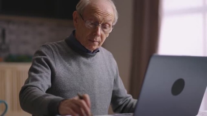 单身老人正在计算自己的费用和计划预算，在厨房工作，使用笔记本电脑和计算器
