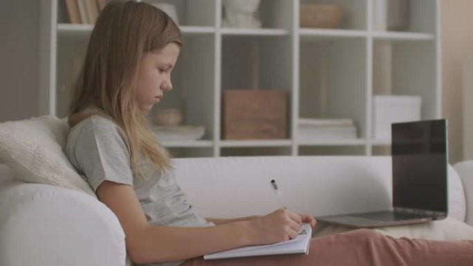 十几岁的女孩放学后在公寓的房间里做作业，写练习本，坐在沙发上，为学童进行电子学习