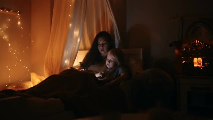 妈妈和小女儿在睡前读童话故事，女人和女孩躺在黑暗的卧室里