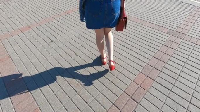 穿着牛仔裙的年轻女孩的腿沿着人行道行走