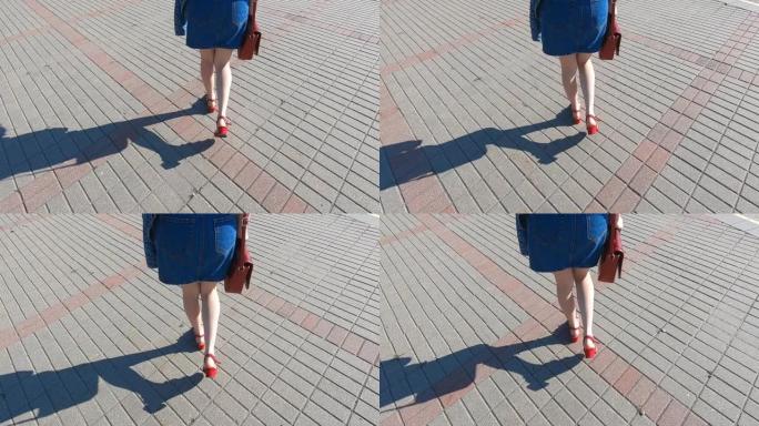 穿着牛仔裙的年轻女孩的腿沿着人行道行走