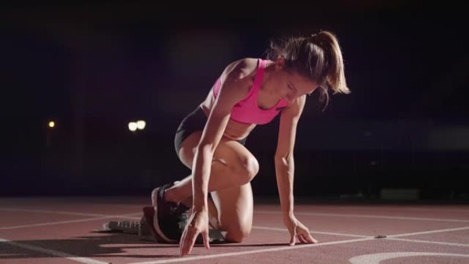 女人在比赛开始时蹲在起跑位上。女运动员准备并开始。跑步者在起跑线前的起点处等待。