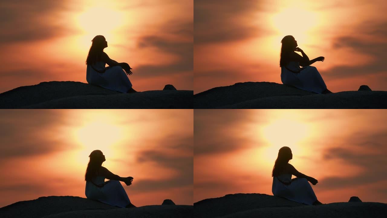 日落时在山顶上放松的年轻女子