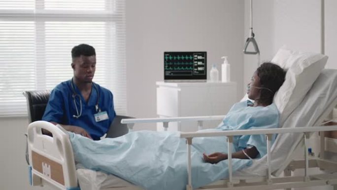 一名男医生正在医院病房里与躺在病床上的病人交谈。连接到氧气和面罩。