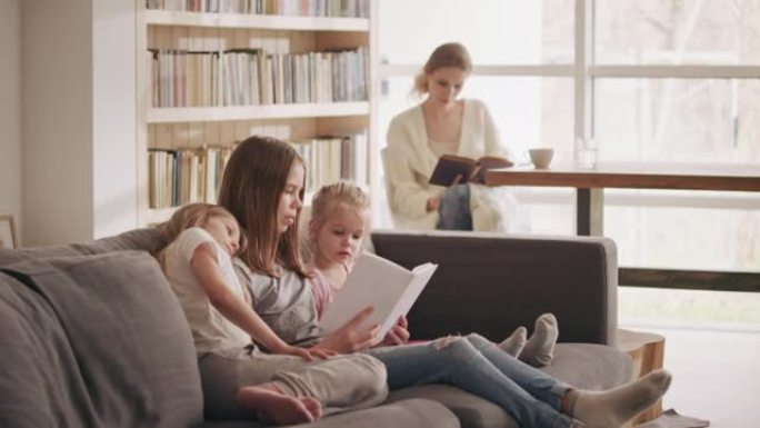 家庭阅读时间。母亲拿着书，照顾三个女儿。女孩在沙发上看书