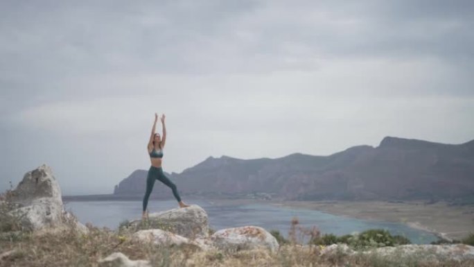年轻女子在海滩附近的悬崖上的岩石上做瑜伽