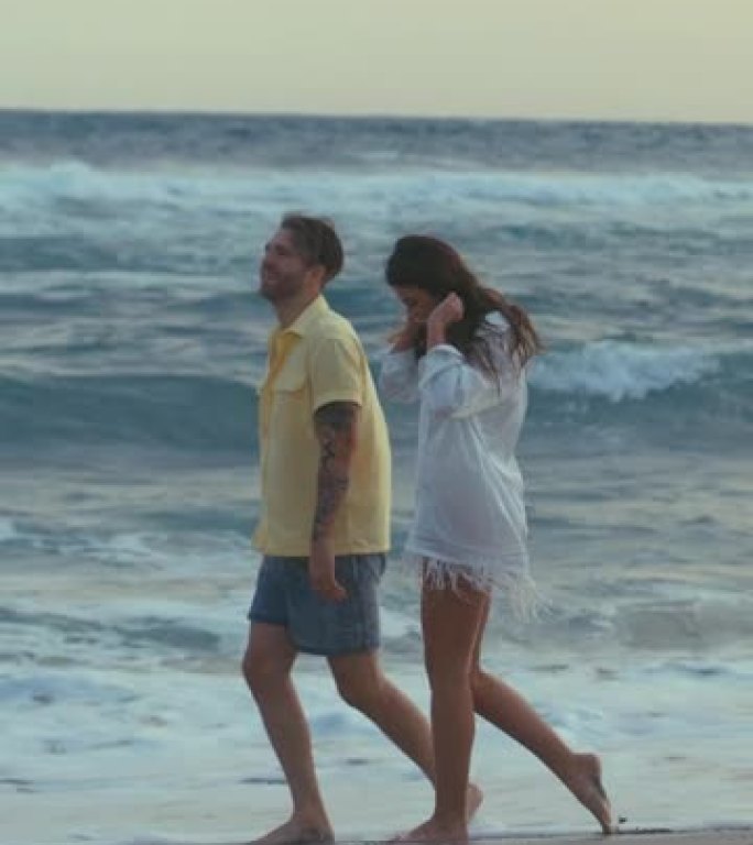 海滩上的浪漫情侣。相爱的情侣手牵着手，在垂直视频周围开玩笑