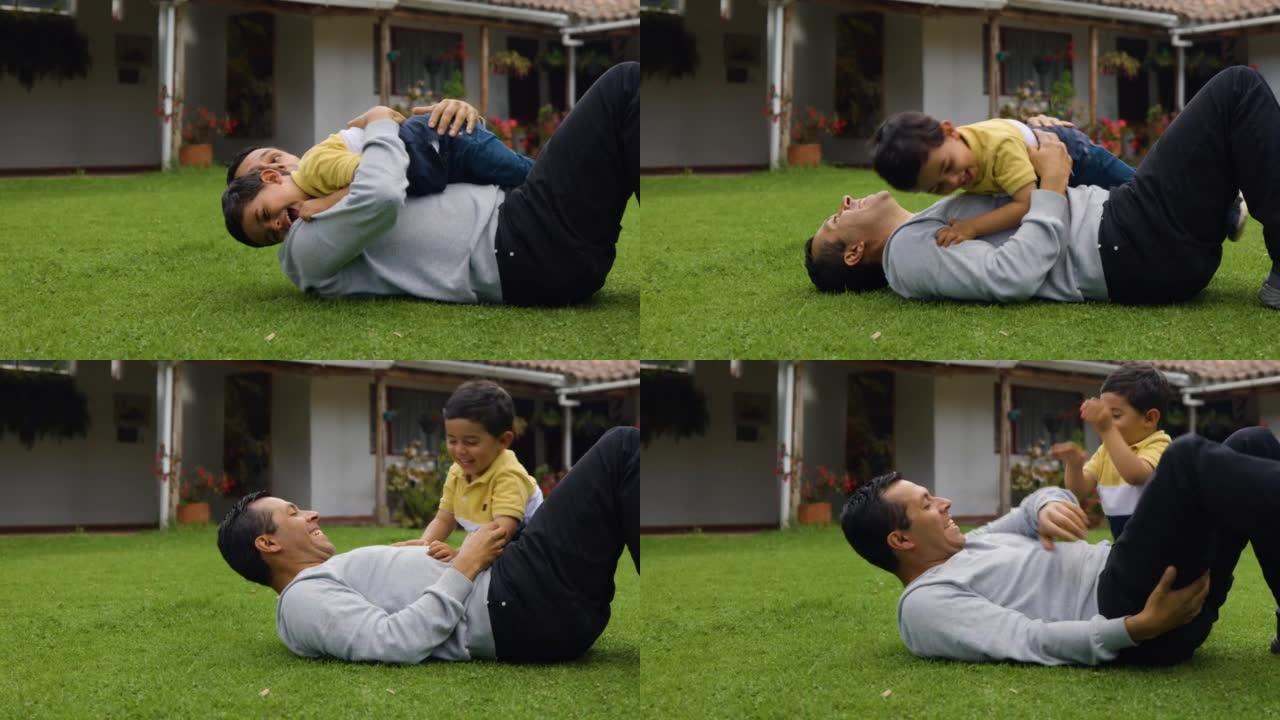 Playful daddy lying down on grass and cute son on 